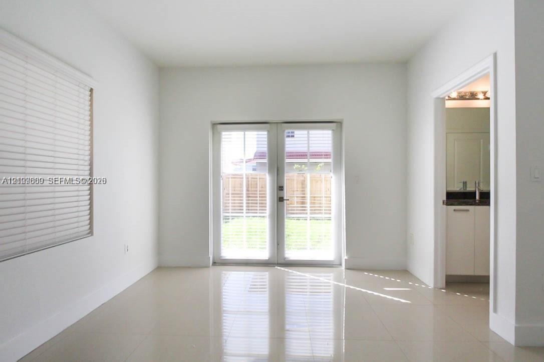 Neutral-toned tile flooring, white walls, horizontal window blinds, and glass-paneled double doors
