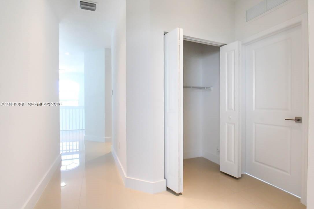 Hallway featuring polished tile flooring, white bi-fold closet doors, a solid-core panel door with a brushed nickel lever handle, and smooth-finish wa