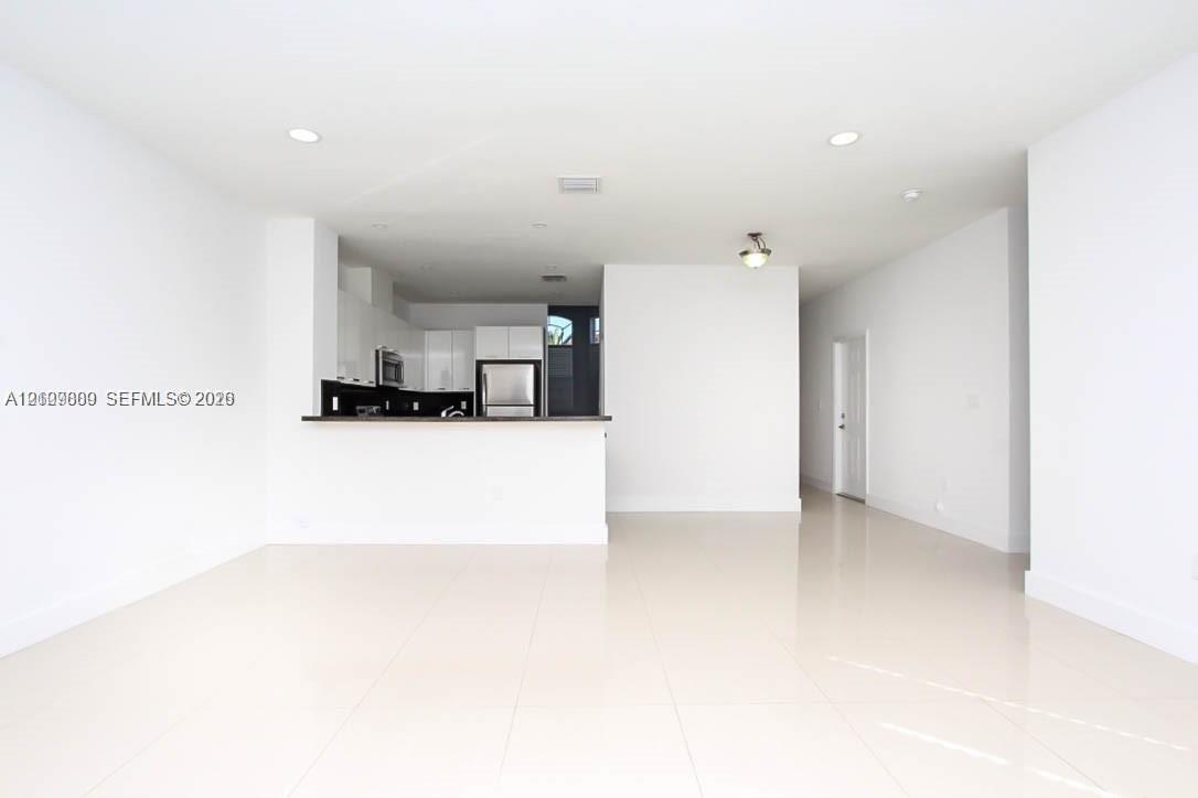 Open-concept interior featuring large-format tile flooring, recessed ceiling lighting, and a breakfast bar with high-gloss cabinetry