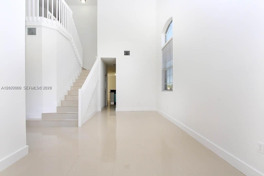 Double-height ceilings featuring an arched window, large-format tile flooring, and a white staircase with a matching balustrade