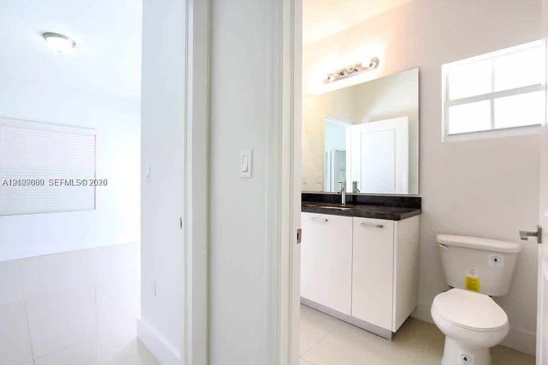 Bathroom featuring a vanity with dark stone countertop, rectangular undermount sink, wall-spanning mirror, multi-bulb vanity light, and polished tile 