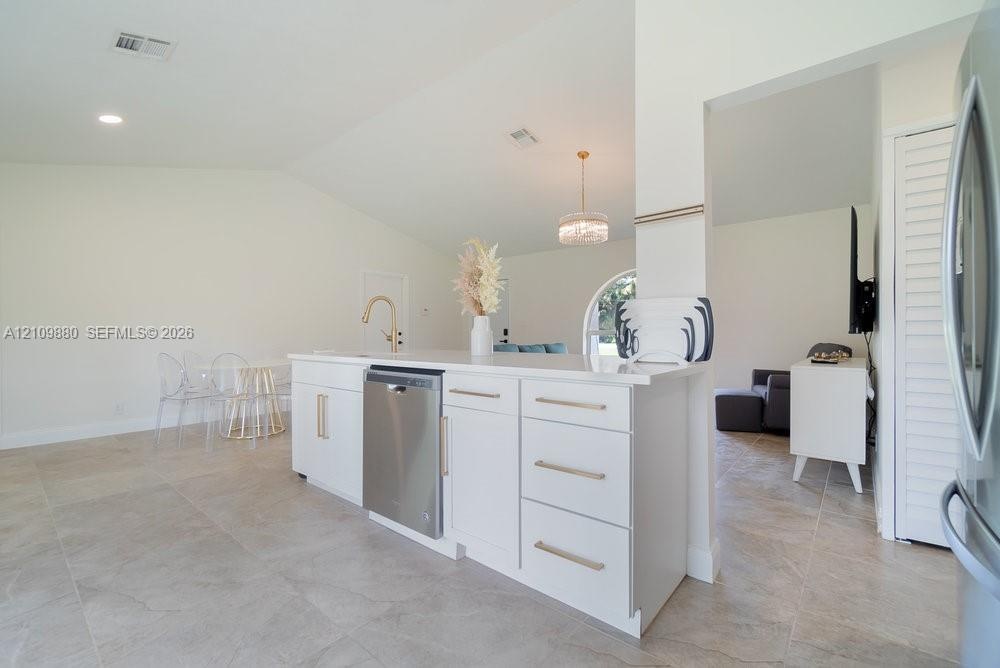 Kitchen island featuring white shaker-style cabinetry, quartz countertops, a brass faucet, and a stainless steel dishwasher, complemented by tile floo