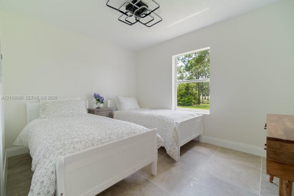 Neutral-toned room featuring large-format tile flooring, a geometric flush-mount ceiling light fixture, and a single-hung window with exterior tree-li