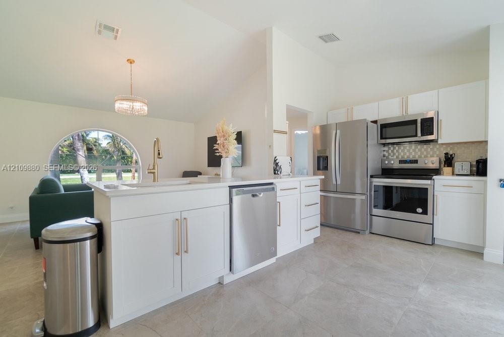 Kitchen featuring white shaker cabinetry, stainless steel appliances, large-format tile flooring, a breakfast bar, and a vaulted ceiling with a circul