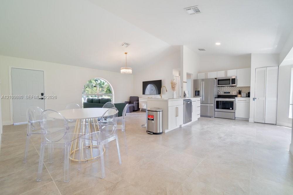 Open floor plan featuring vaulted ceilings, neutral large-format tile flooring, a kitchen island with white cabinetry, stainless steel appliances, and