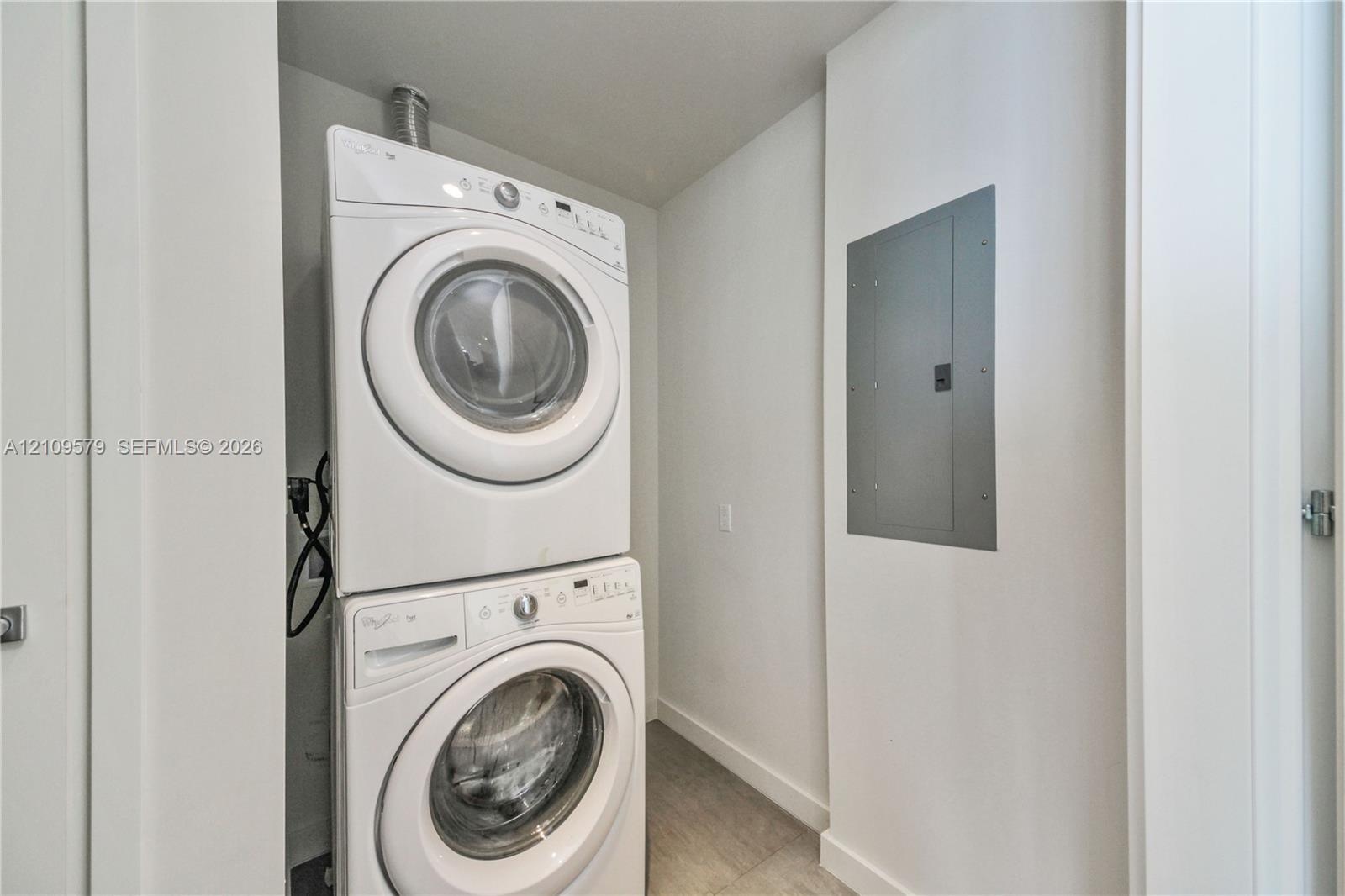 Dedicated laundry area featuring a stacked washer and dryer set and a recessed electrical service panel