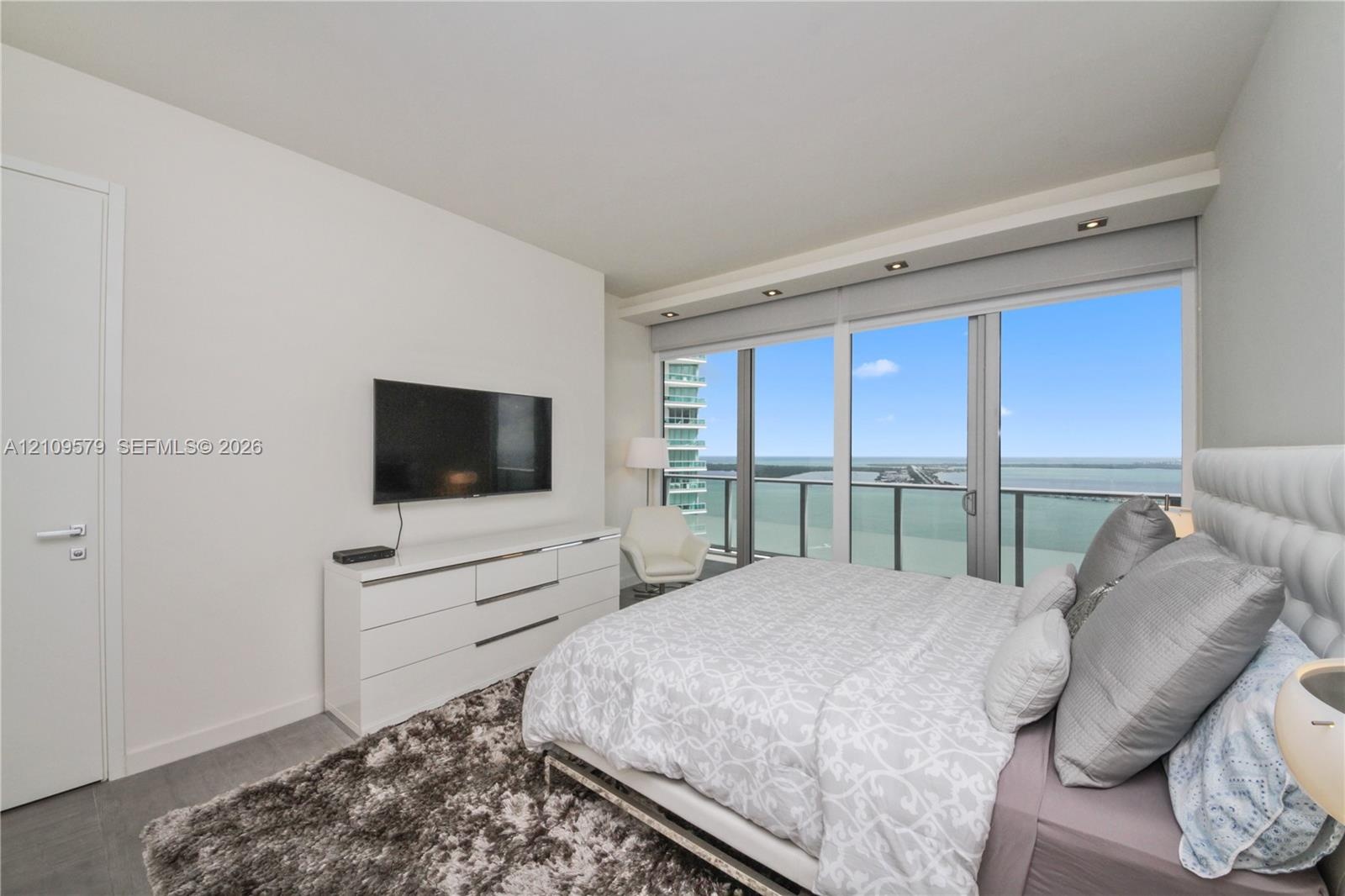 Floor-to-ceiling sliding glass doors, recessed lighting, and water-facing balcony access