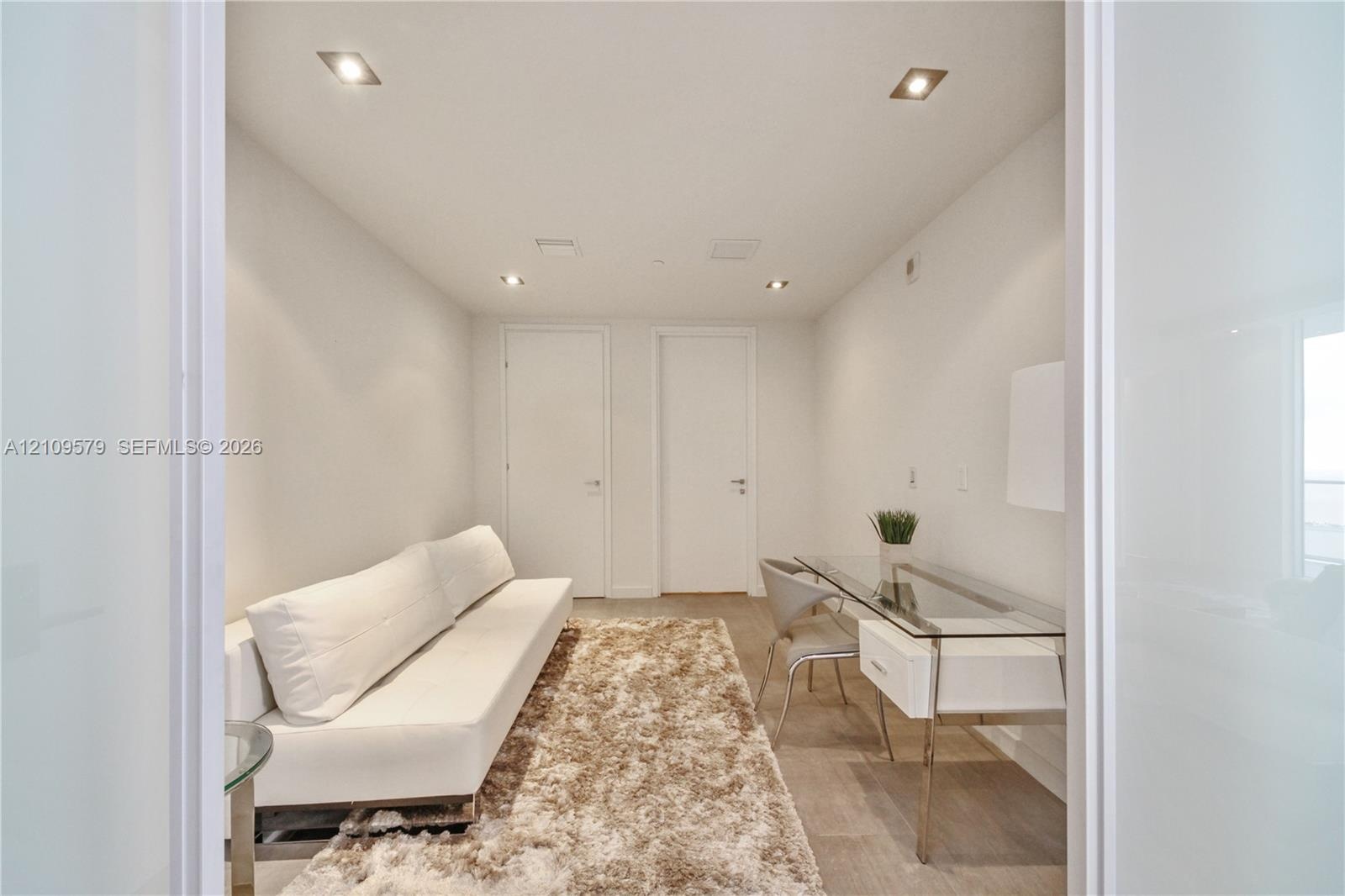 Neutral-toned interior space featuring recessed ceiling lighting, wood-finish flooring, and two interior doors