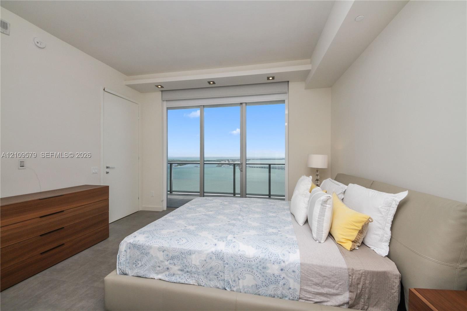 Floor-to-ceiling sliding glass door, recessed ceiling lighting, neutral wall finishes, grey tile flooring, and water backdrop