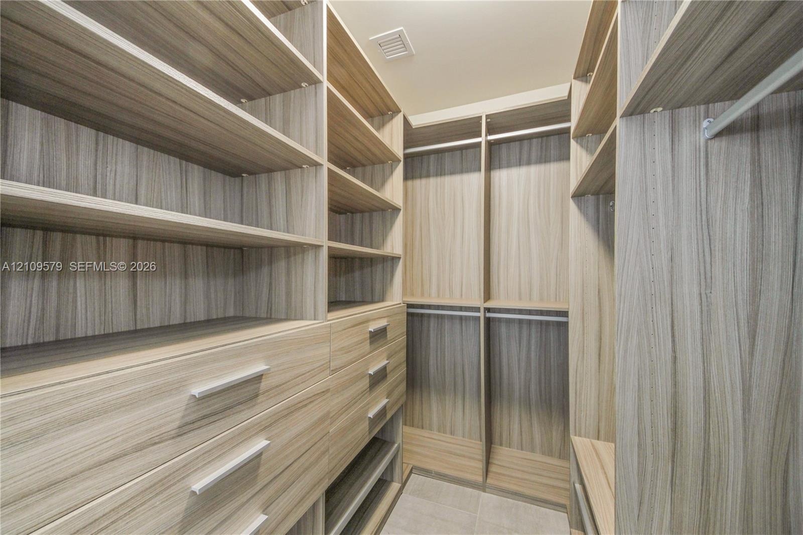 Walk-in closet featuring custom wood-finish cabinetry, built-in shelving, multiple pull-out drawers with metal hardware, and dual hanging rods
