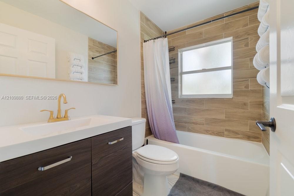 Bathroom featuring a vanity with wood-finish cabinetry, a white integrated countertop, brass-tone faucet, large wall-mounted mirror, and a tub-shower 