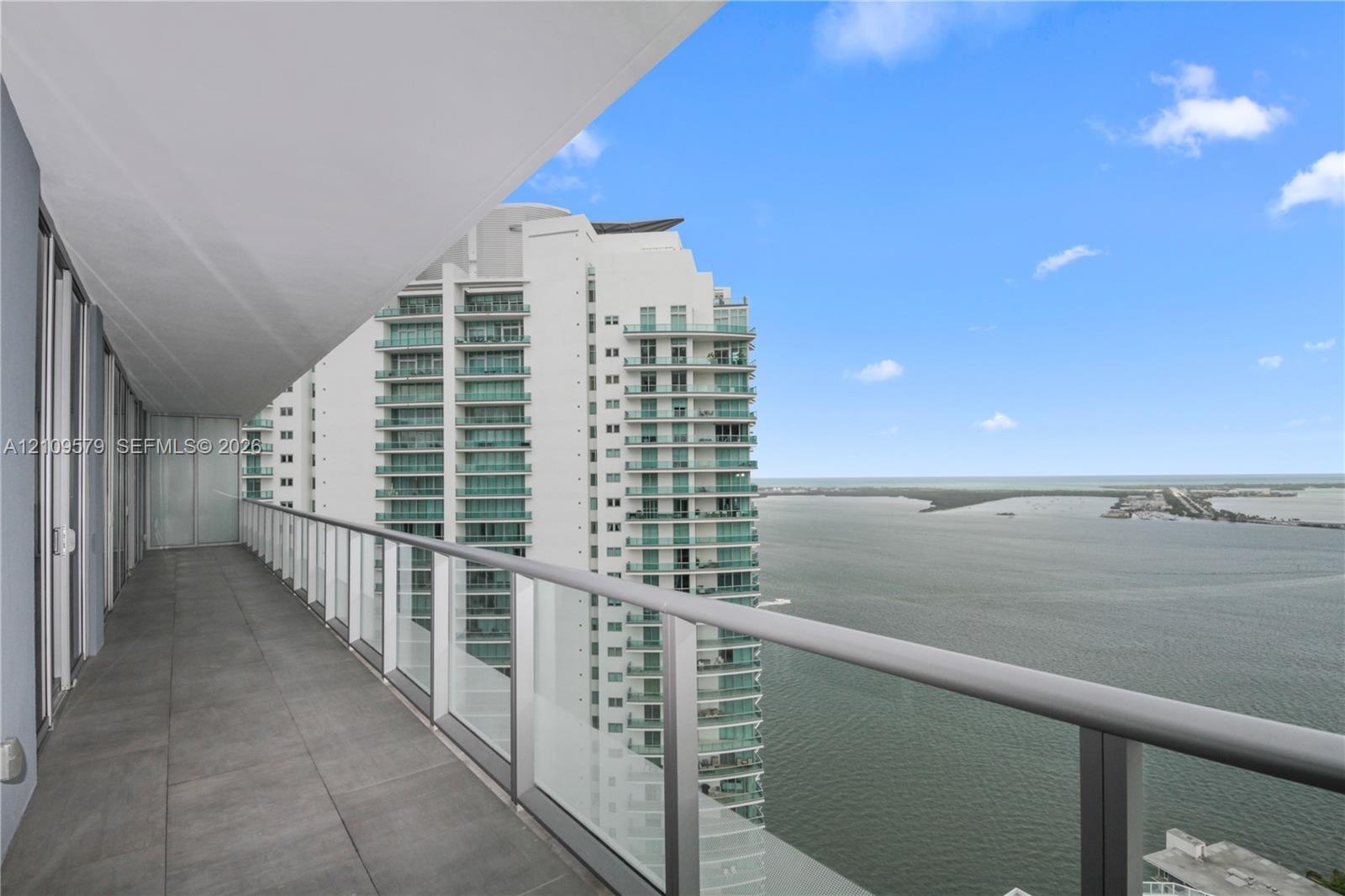 Covered balcony featuring large-format stone tile flooring and a sleek metal railing with glass panels