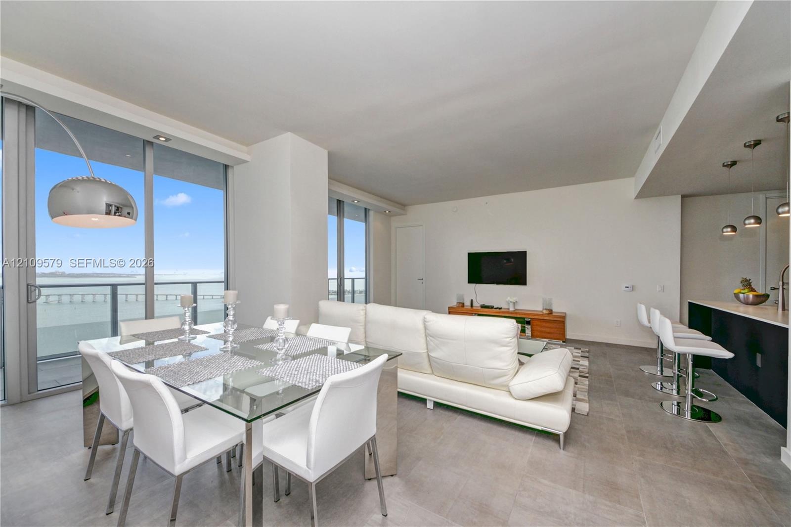Open-concept living space featuring floor-to-ceiling glass doors, stone-finish tile flooring, recessed ceiling lighting, and a kitchen island with a s