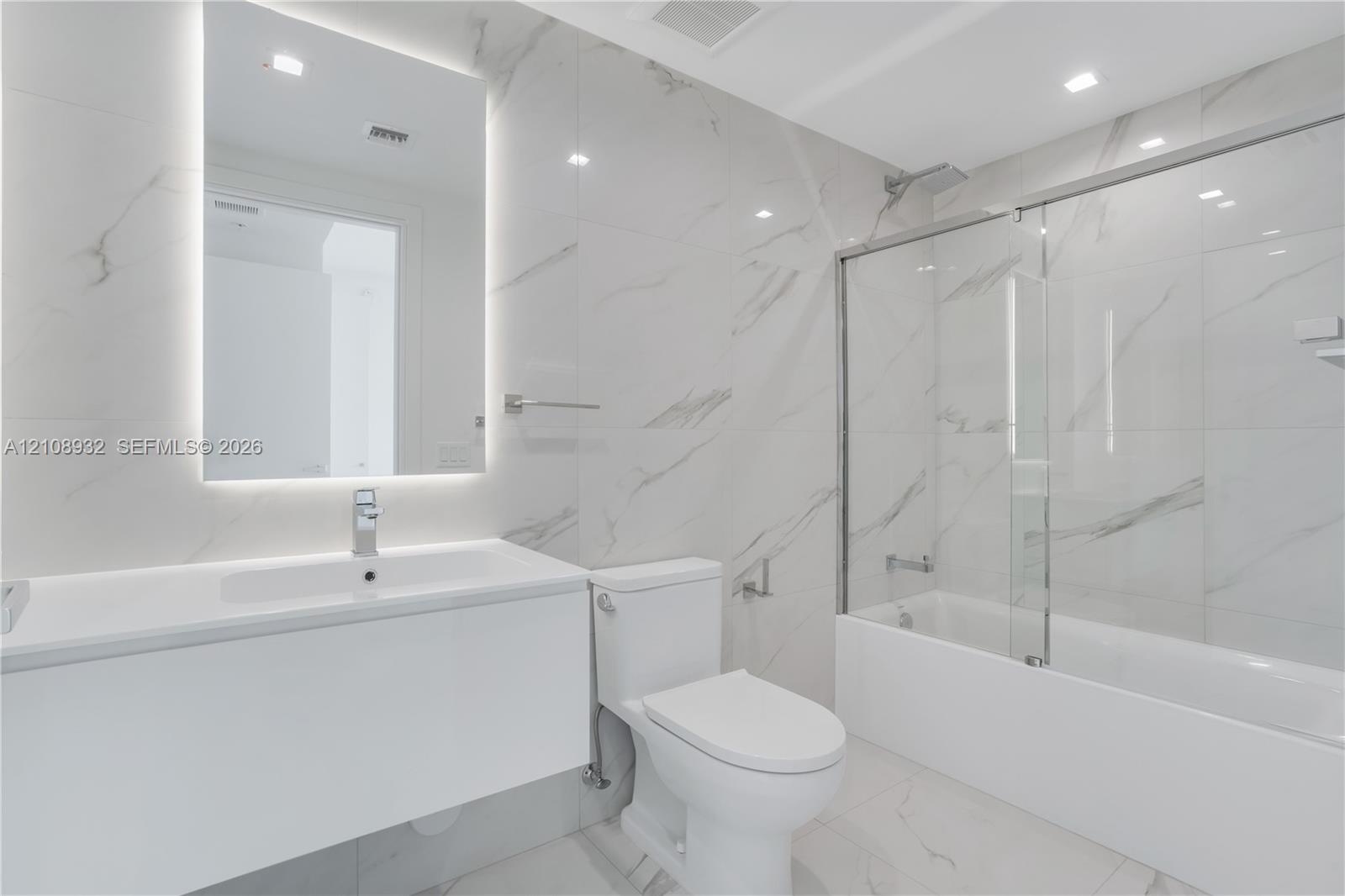 Bathroom featuring large-format stone-patterned wall and floor tile, a modern floating vanity with an integrated sink, a frameless glass tub enclosure