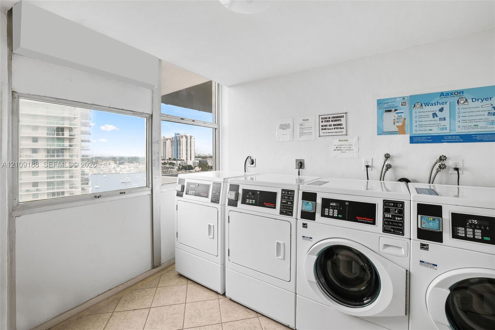 Laundry room featuring ceramic tile flooring, floor-to-ceiling windows, and multiple commercial-grade front-loading washing machines and dryers