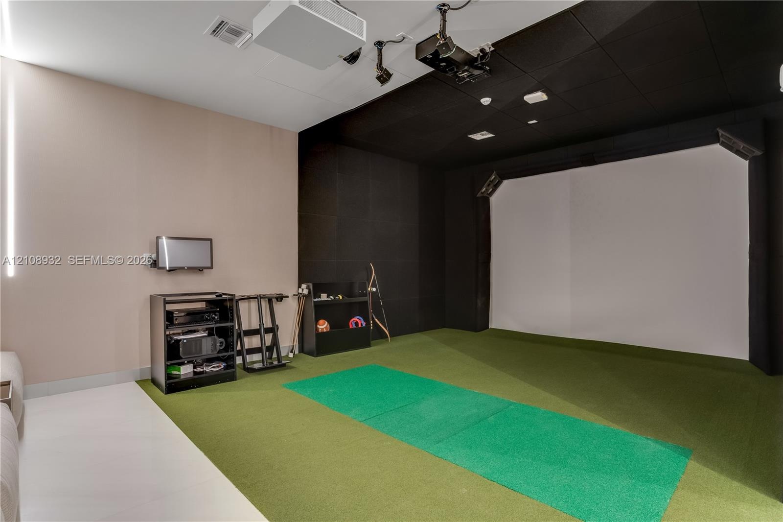 Dedicated simulator room featuring an impact screen, integrated projection system, green turf flooring, and acoustic wall paneling