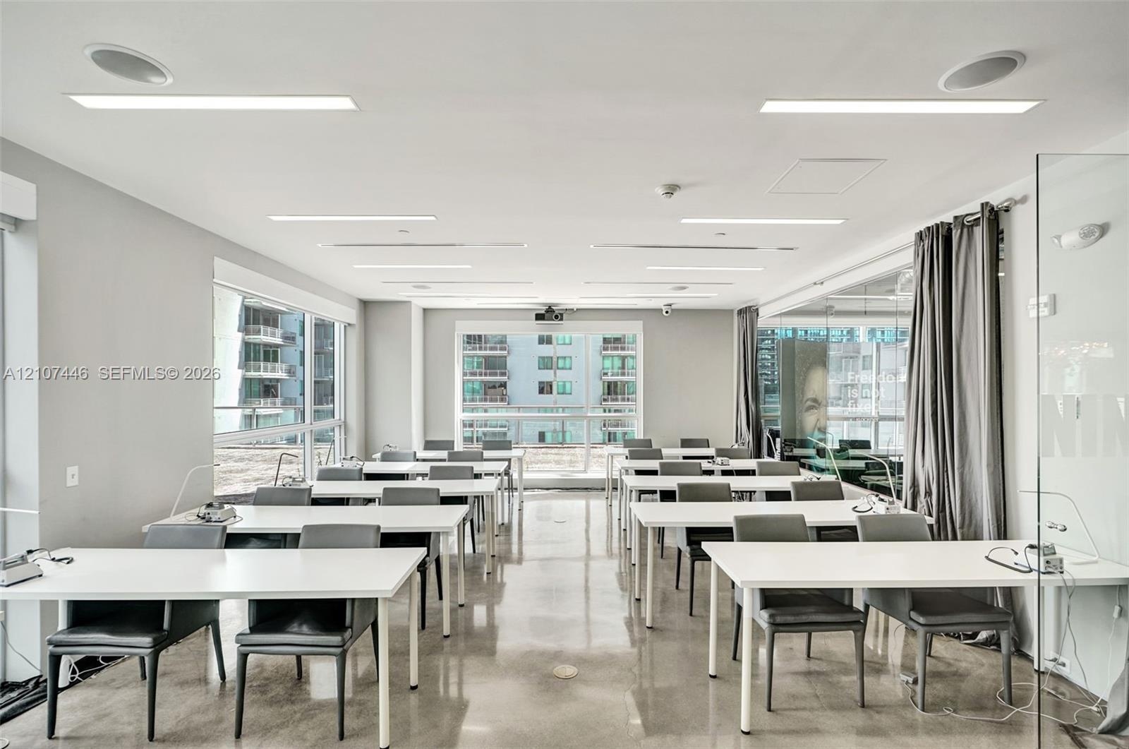 Expansive room featuring polished concrete flooring, recessed linear lighting, integrated ceiling speakers, floor-to-ceiling windows, and glass partit