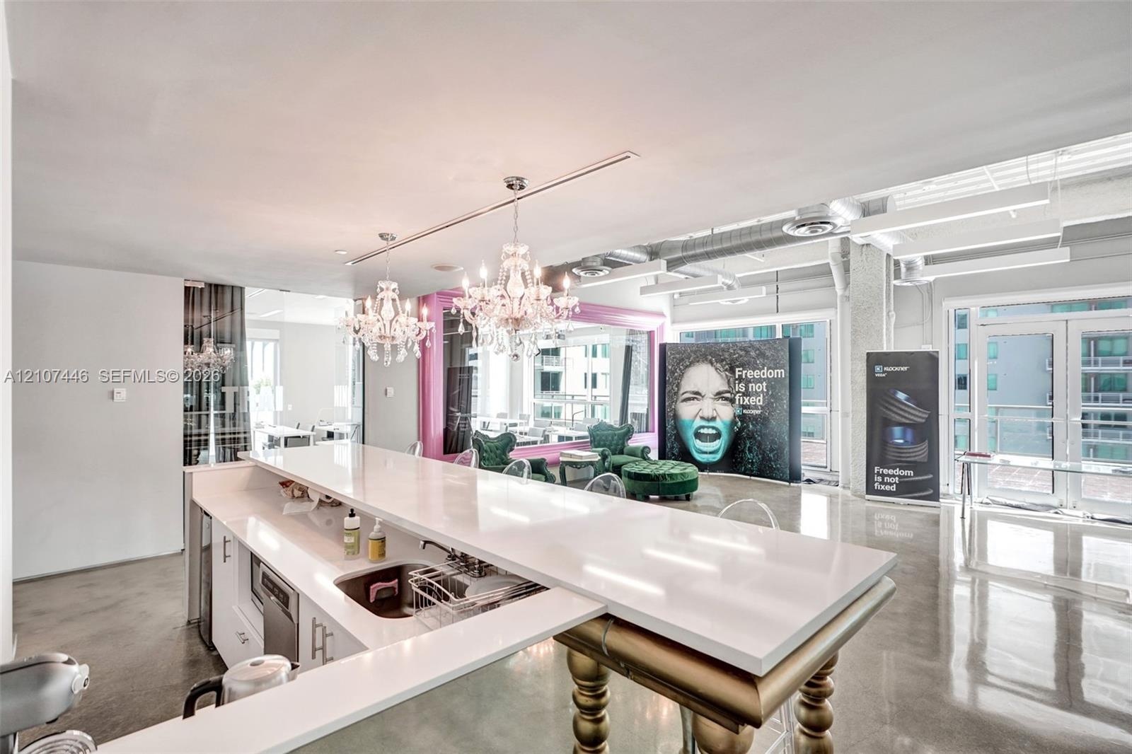 Kitchen island with a white solid-surface countertop and built-in stainless steel sink, paired with two ornate crystal chandeliers and polished concre