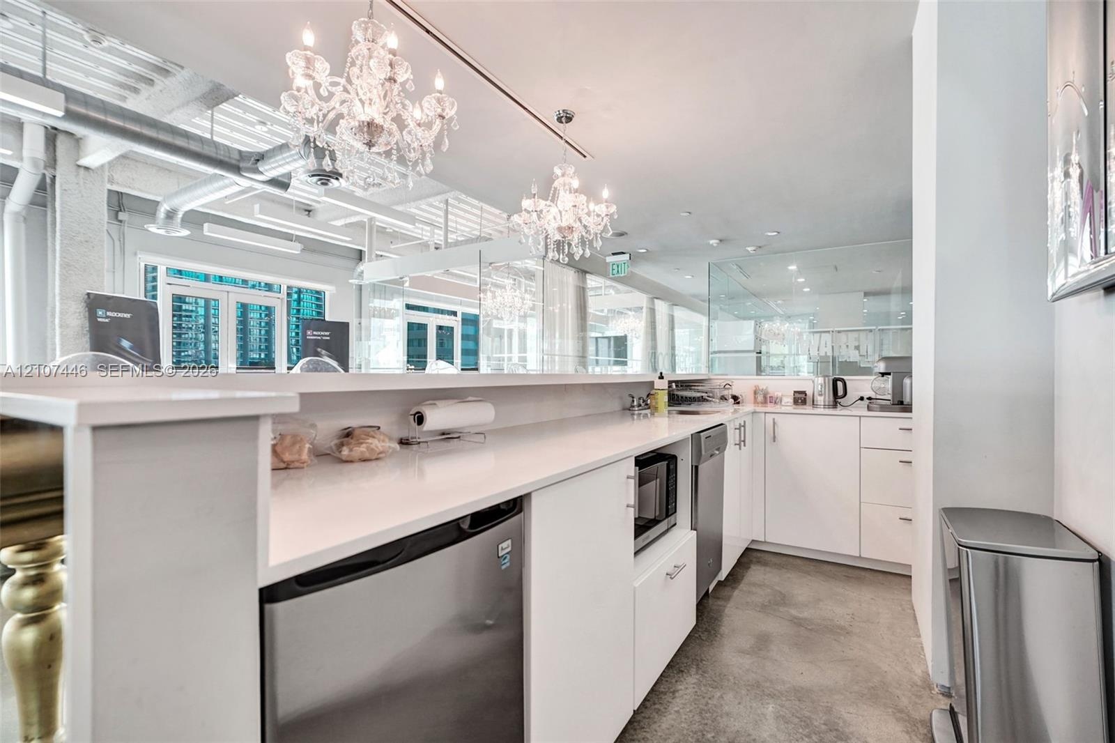 Kitchen area featuring white cabinetry, solid-surface countertops, industrial-style exposed ductwork, polished concrete flooring, and crystal chandeli