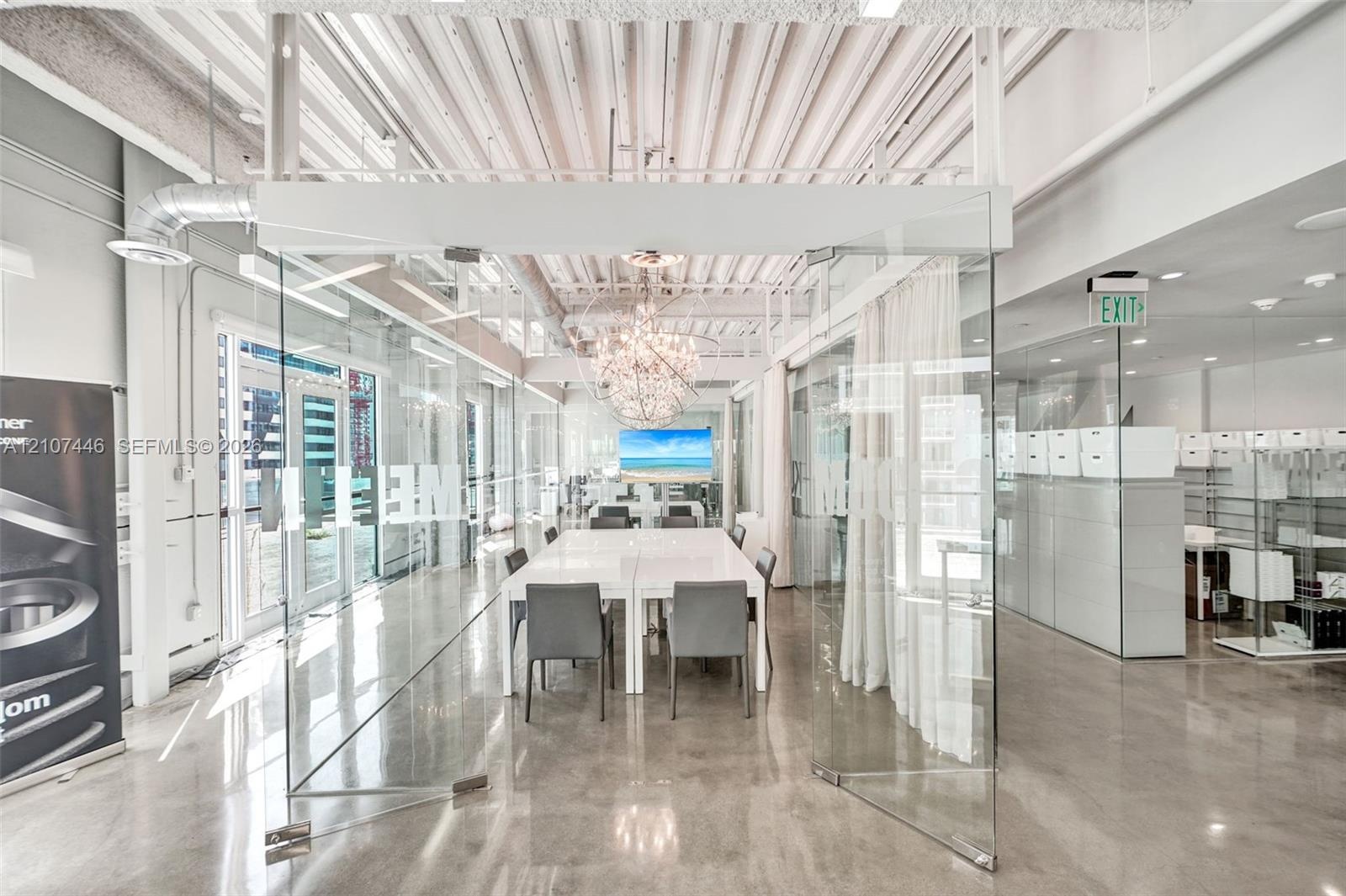 Industrial-style interior featuring high vaulted ceilings with exposed beams, polished concrete flooring, glass-paneled walls, and a large decorative 