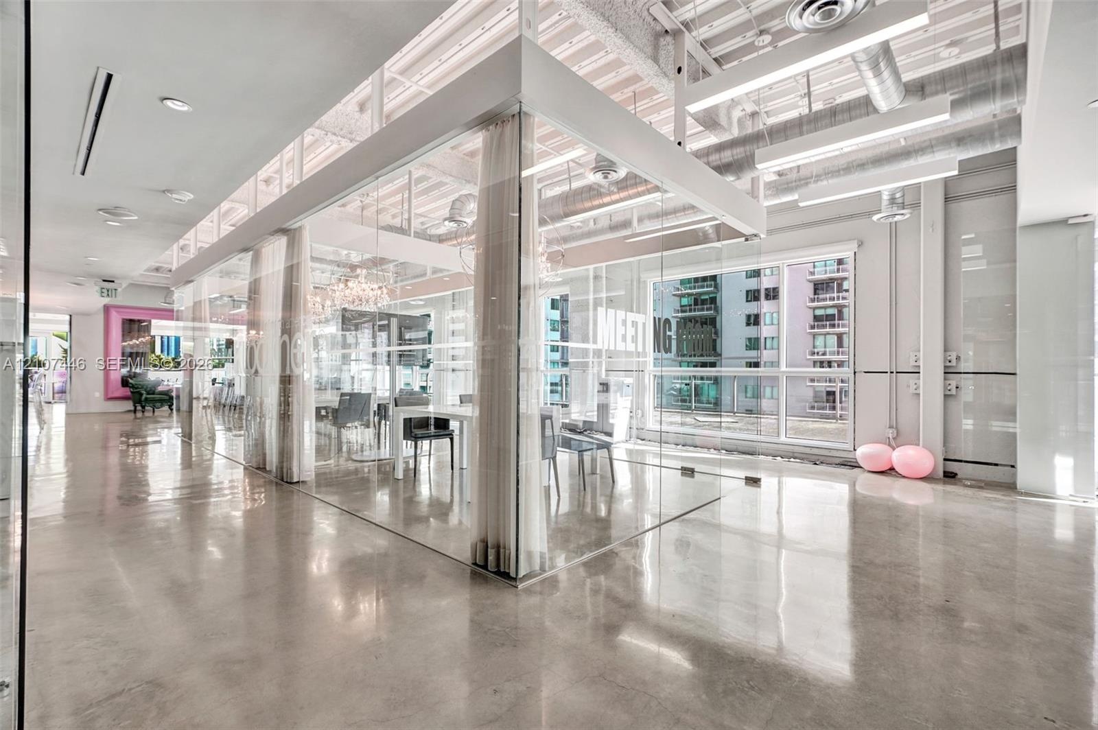 Industrial interior featuring polished concrete flooring, exposed overhead ductwork, floor-to-ceiling glass panel walls, and linear recessed lighting