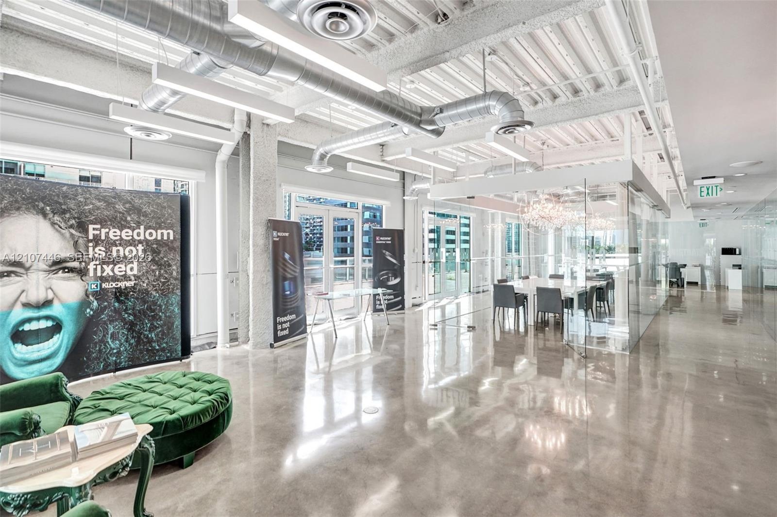 Industrial-style interior featuring polished concrete flooring, exposed overhead ductwork, soaring ceilings with steel beams, and floor-to-ceiling gla