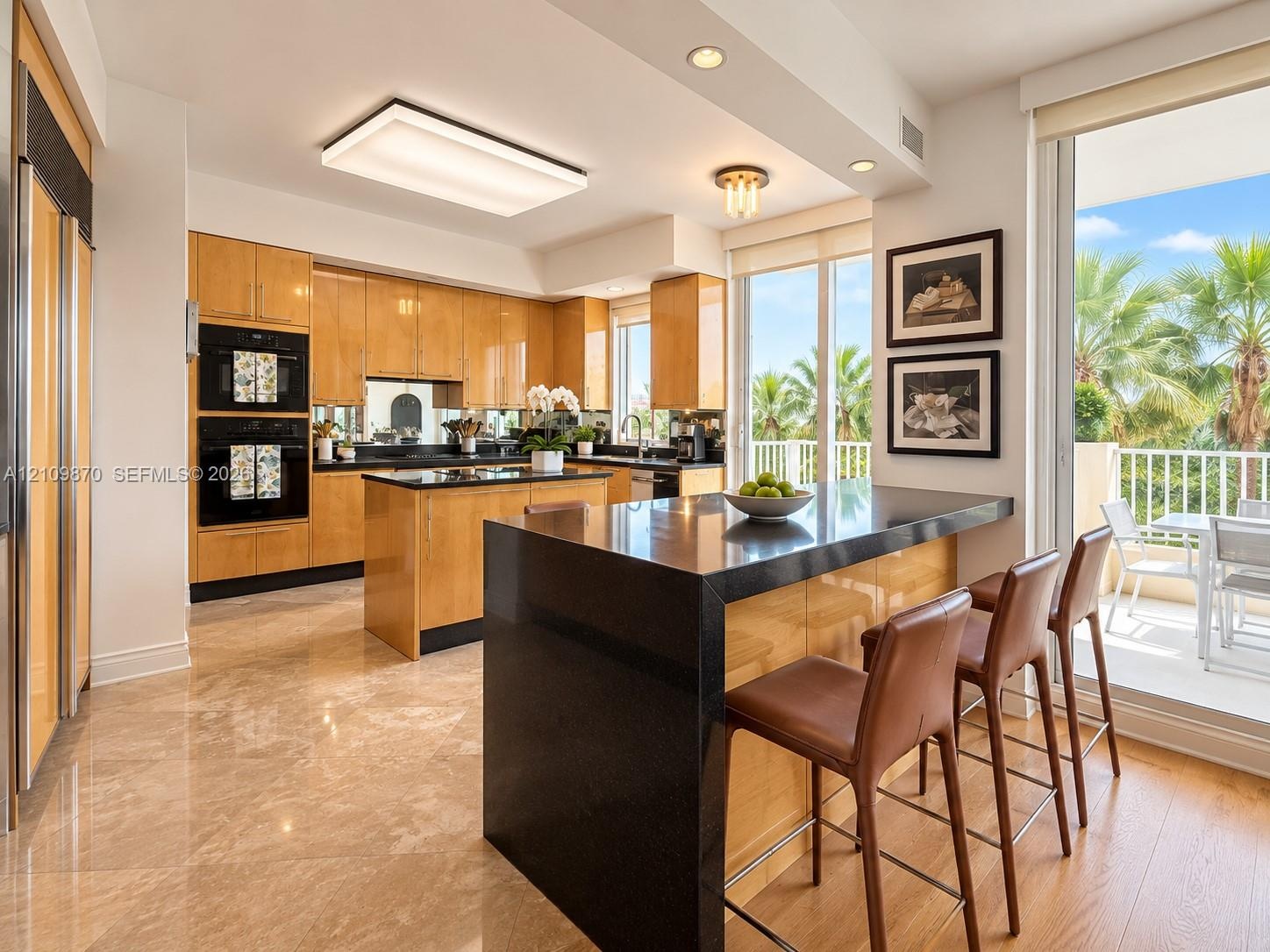 Kitchen featuring flat-panel wood cabinetry, black stone countertops, a central island with a waterfall edge, built-in double ovens, and large-format 