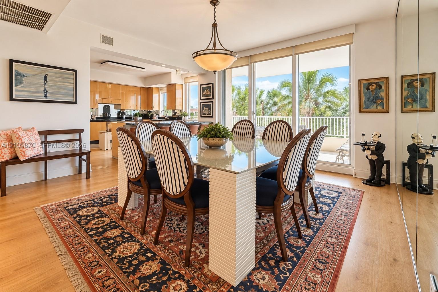 Dining area featuring wood-finish flooring, a tiered semi-flush mount light fixture, full-height mirrored wall paneling, and sliding glass doors with 