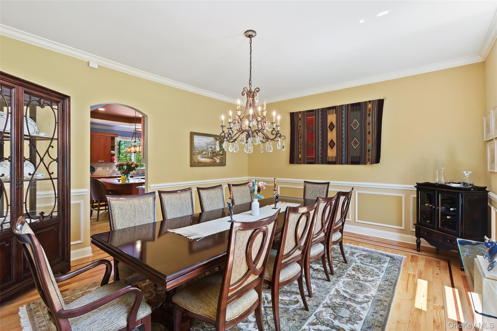 Dining space featuring arched walkways, crown molding, wood finished floors, a chandelier, and a wainscoted wall