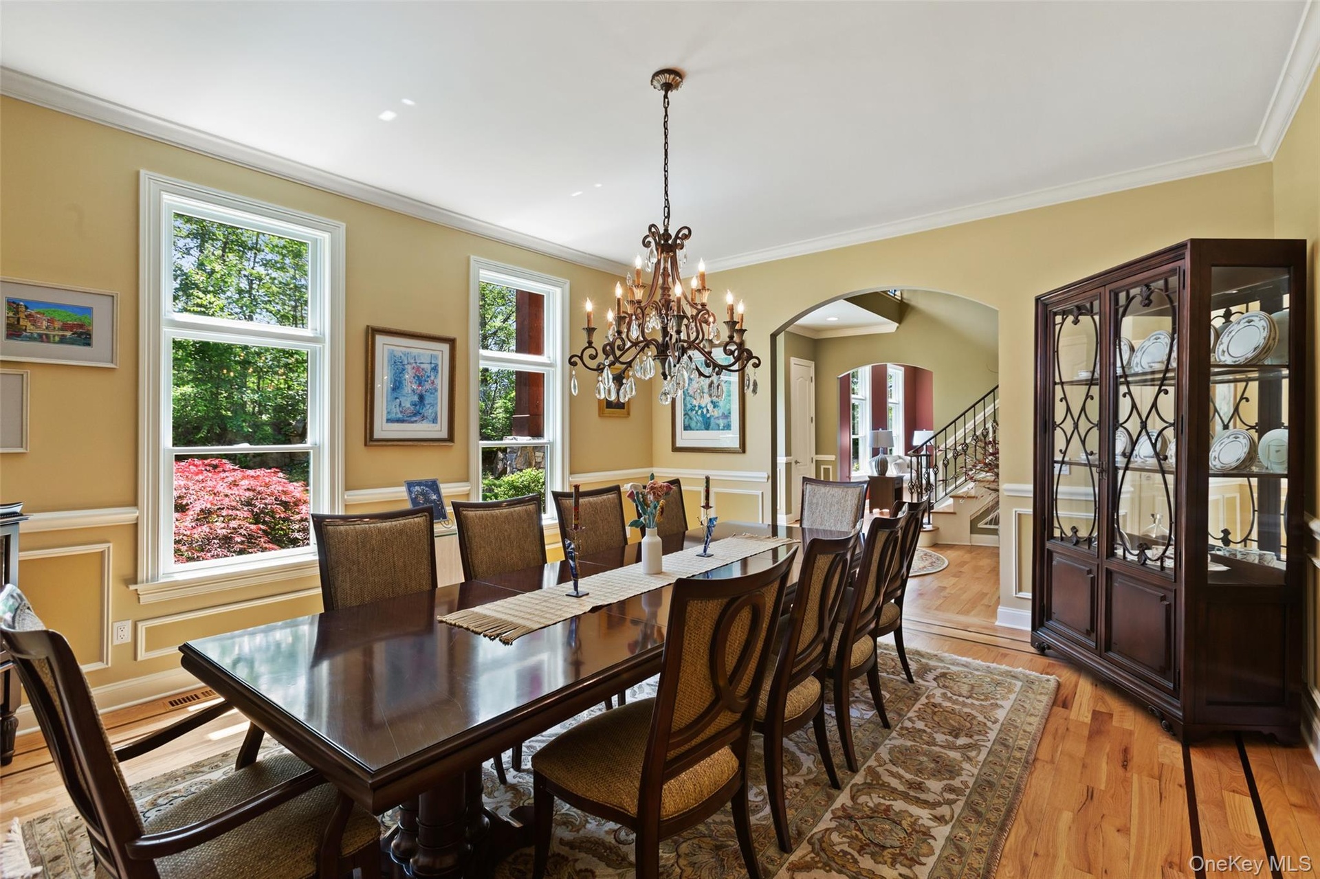 Dining space with arched walkways, light wood finished floors, crown molding, stairway, and wainscoting