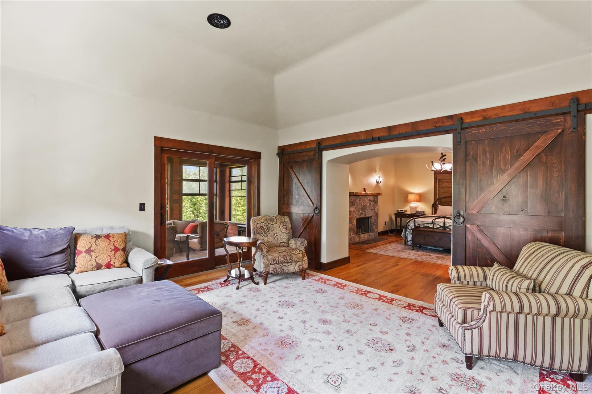Luxurious Primary Bedroom with a barn door, wood finished floors, arched walkways, and high vaulted ceiling