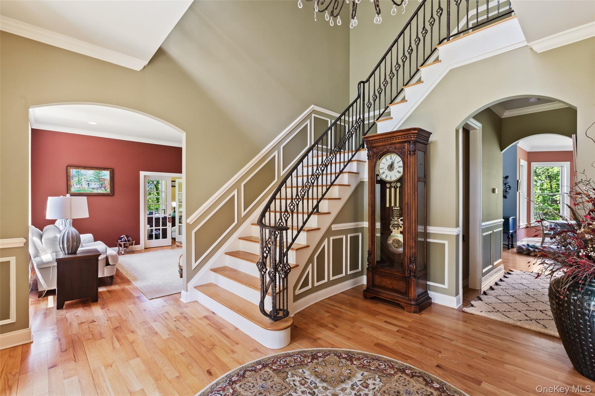 Stairway with wood finished floors, healthy amount of natural light, arched walkways, ornamental molding, and a towering ceiling