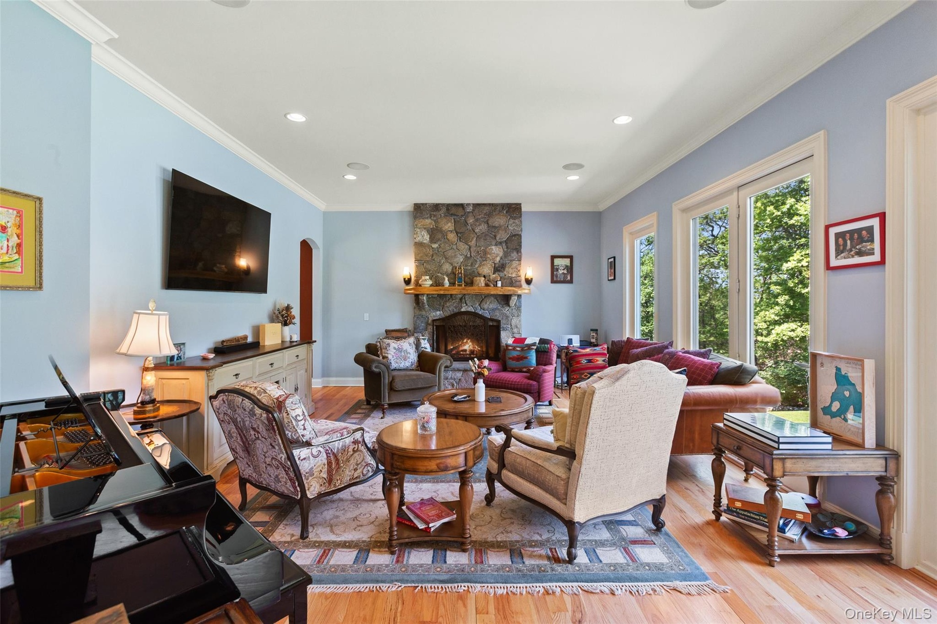 Living area featuring a stone fireplace, light wood-type flooring, recessed lighting, crown molding, and arched walkways