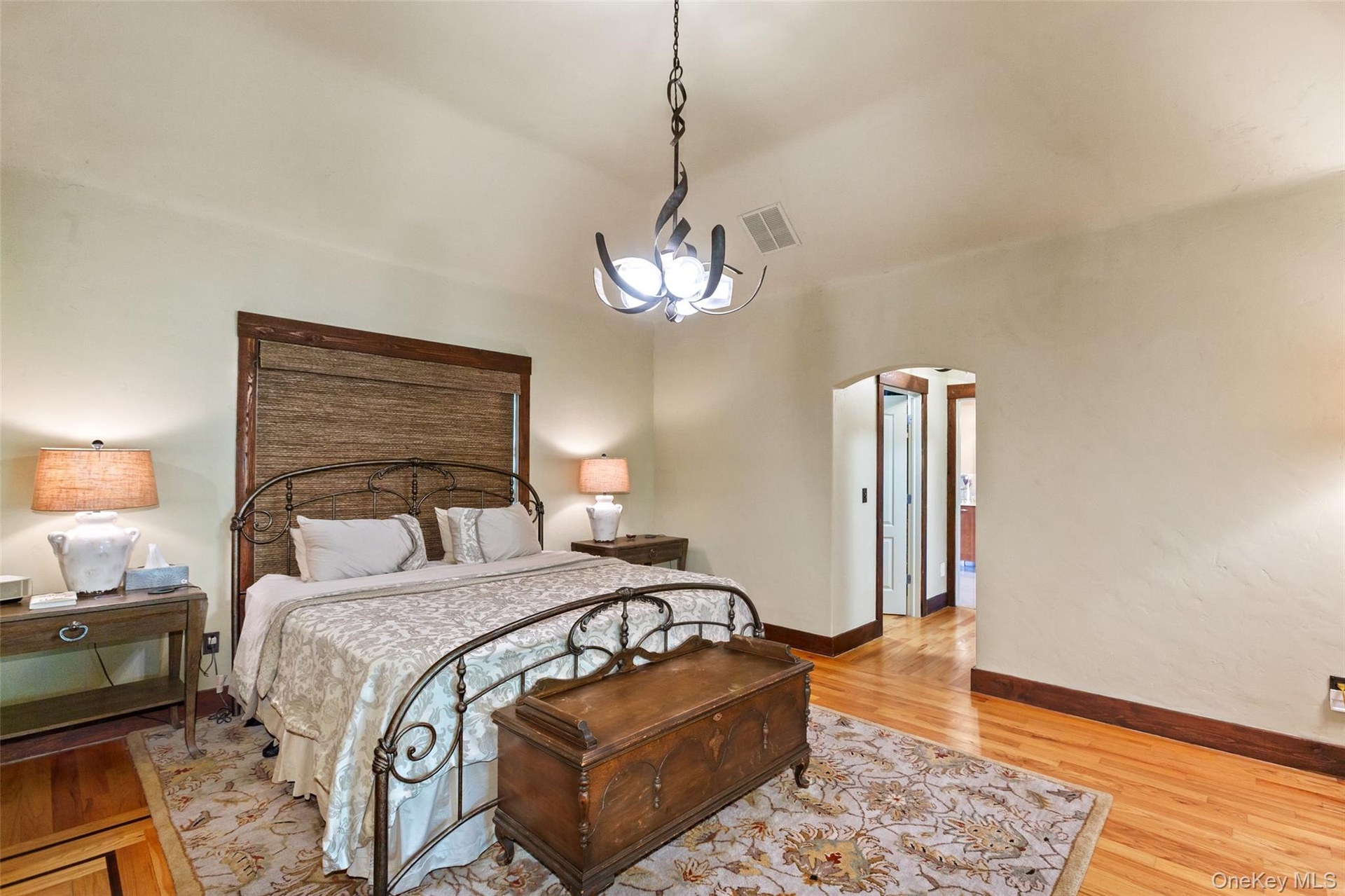 Bedroom featuring arched walkways, light wood-style floors, baseboards, high vaulted ceiling, and a chandelier