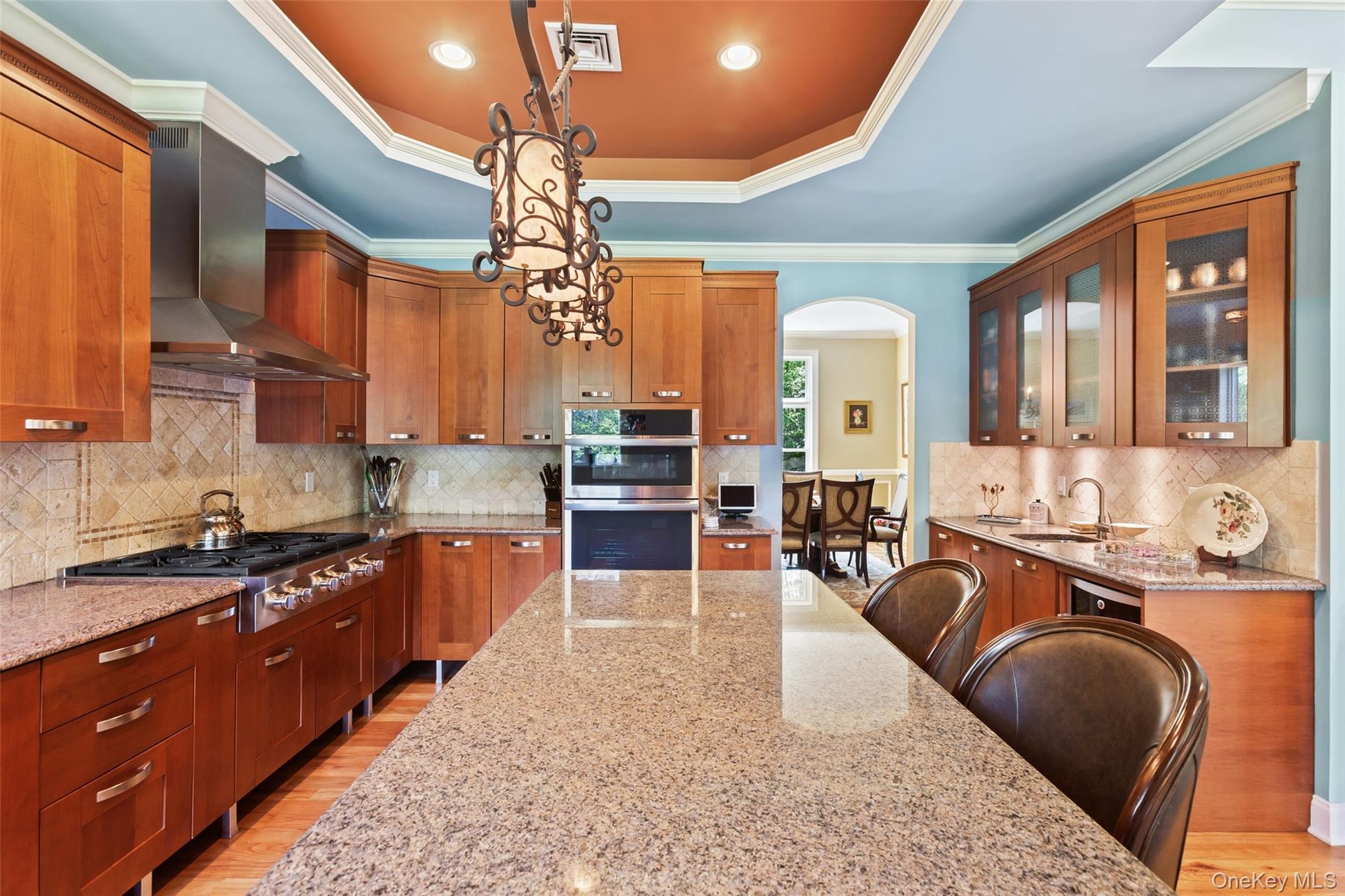 Kitchen featuring stainless steel appliances, arched walkways, wall chimney range hood, light wood-type flooring, and light stone counters