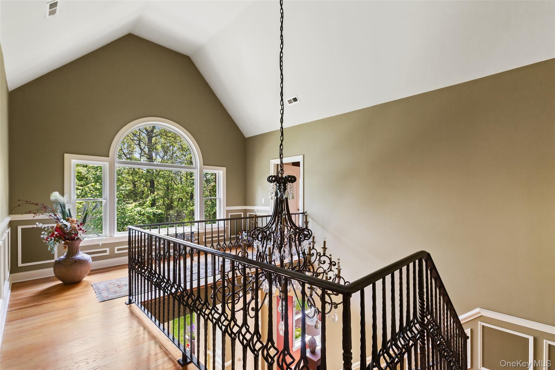 Stairs with high vaulted ceiling, a chandelier, wood finished floors, and a wainscoted wall