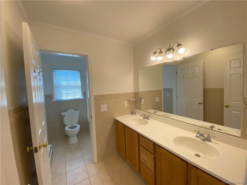 Bathroom featuring dual vanity, tile walls, crown molding, toilet, and tile patterned floors
