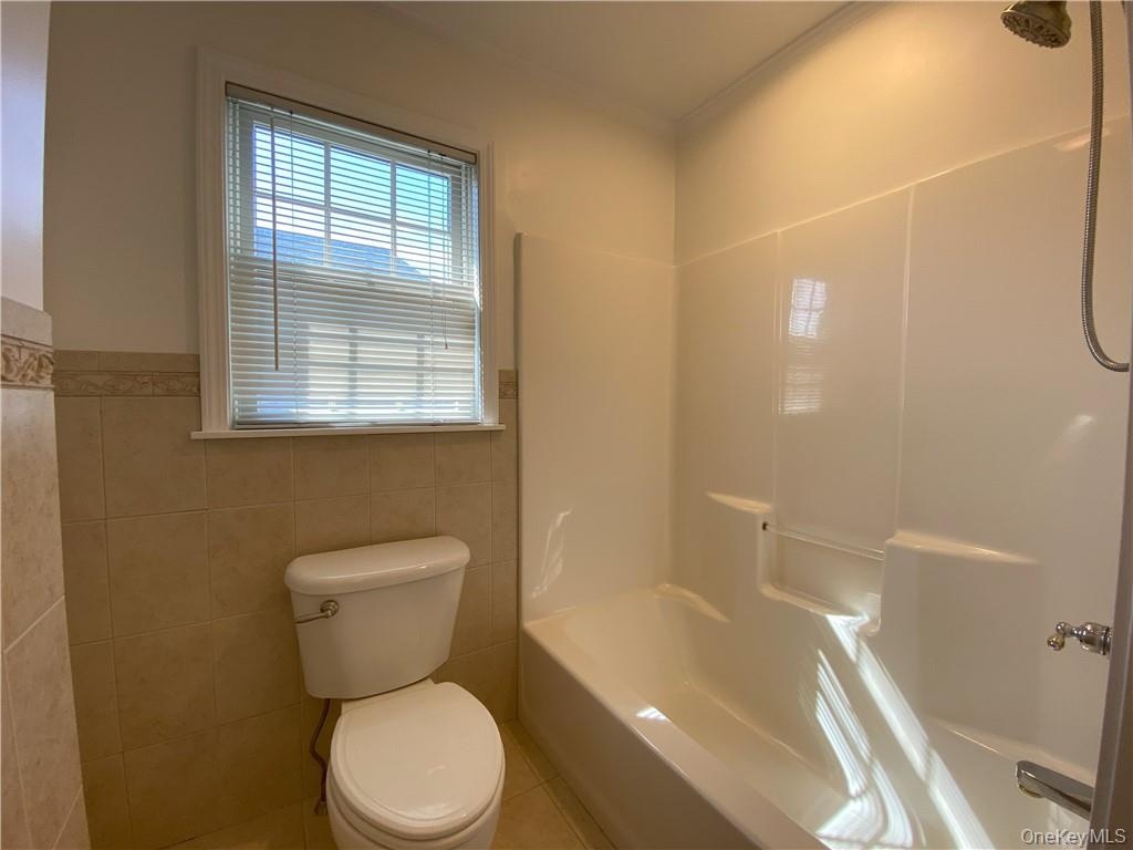 Bathroom with tile patterned floors, shower / washtub combination, tile walls, and toilet