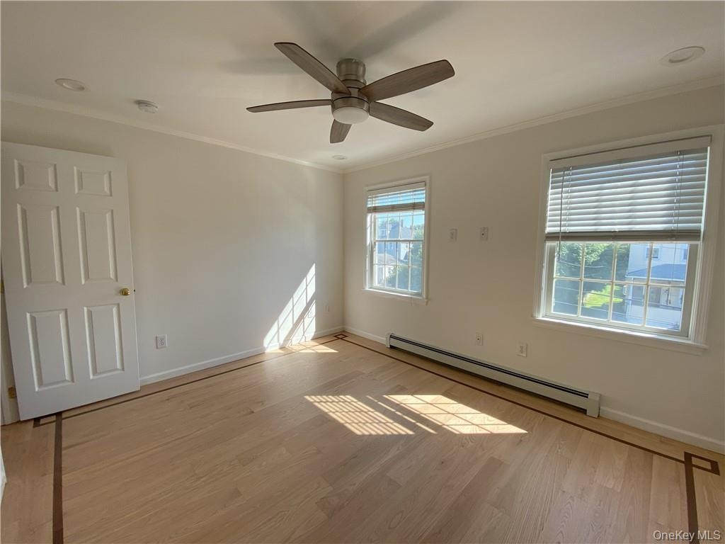 Empty room featuring a baseboard radiator, ceiling fan, light wood-type flooring, and crown molding