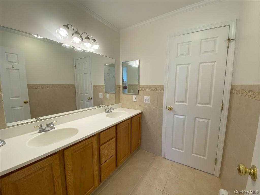 Bathroom with ornamental molding, tile walls, dual bowl vanity, and tile patterned flooring