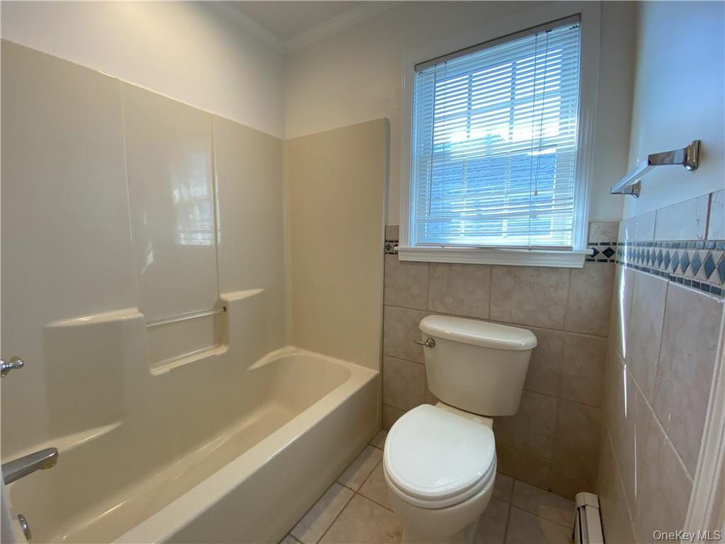 Bathroom featuring tile patterned flooring, tile walls, shower / bathing tub combination, and toilet
