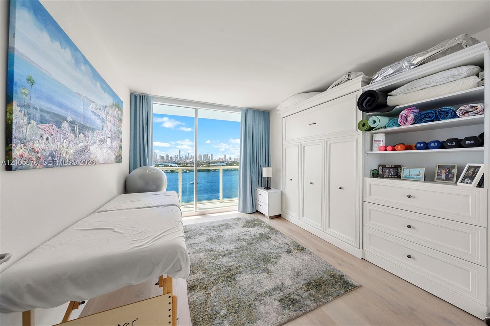 Floor-to-ceiling sliding glass door, custom built-in white cabinetry, wood-finish flooring, and expansive water and skyline backdrop