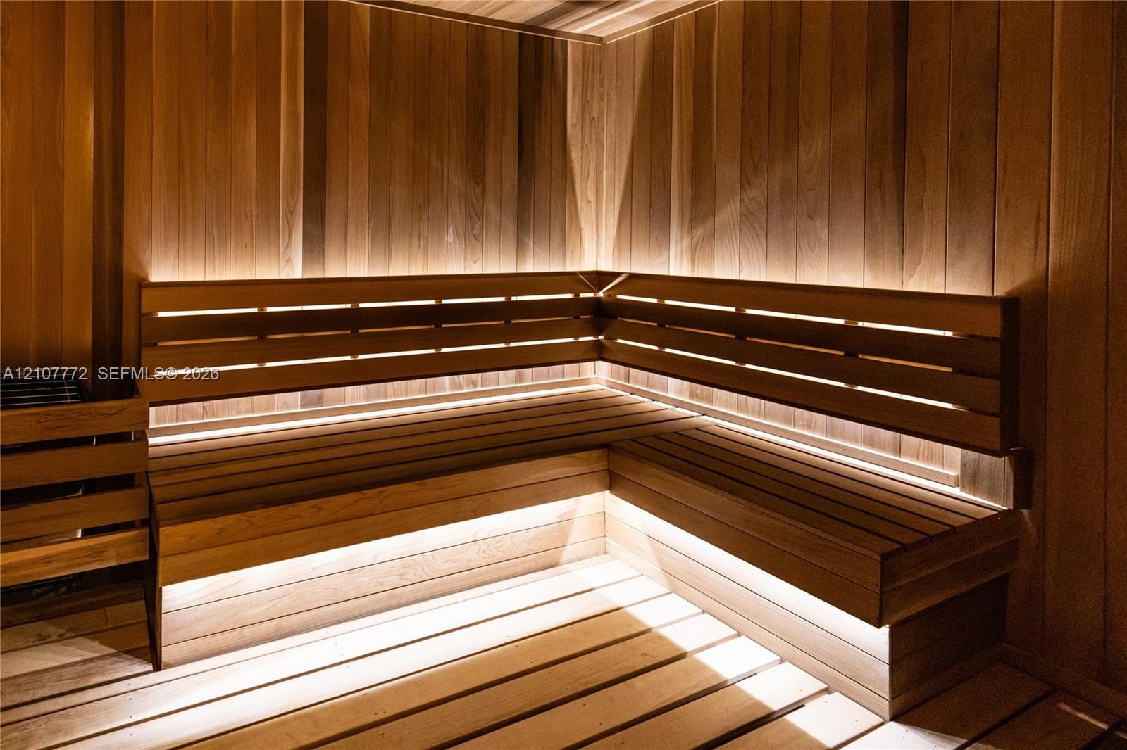 Custom cedar-paneled sauna featuring tiered L-shaped benches, integrated linear accent lighting, and a wall-mounted heater unit