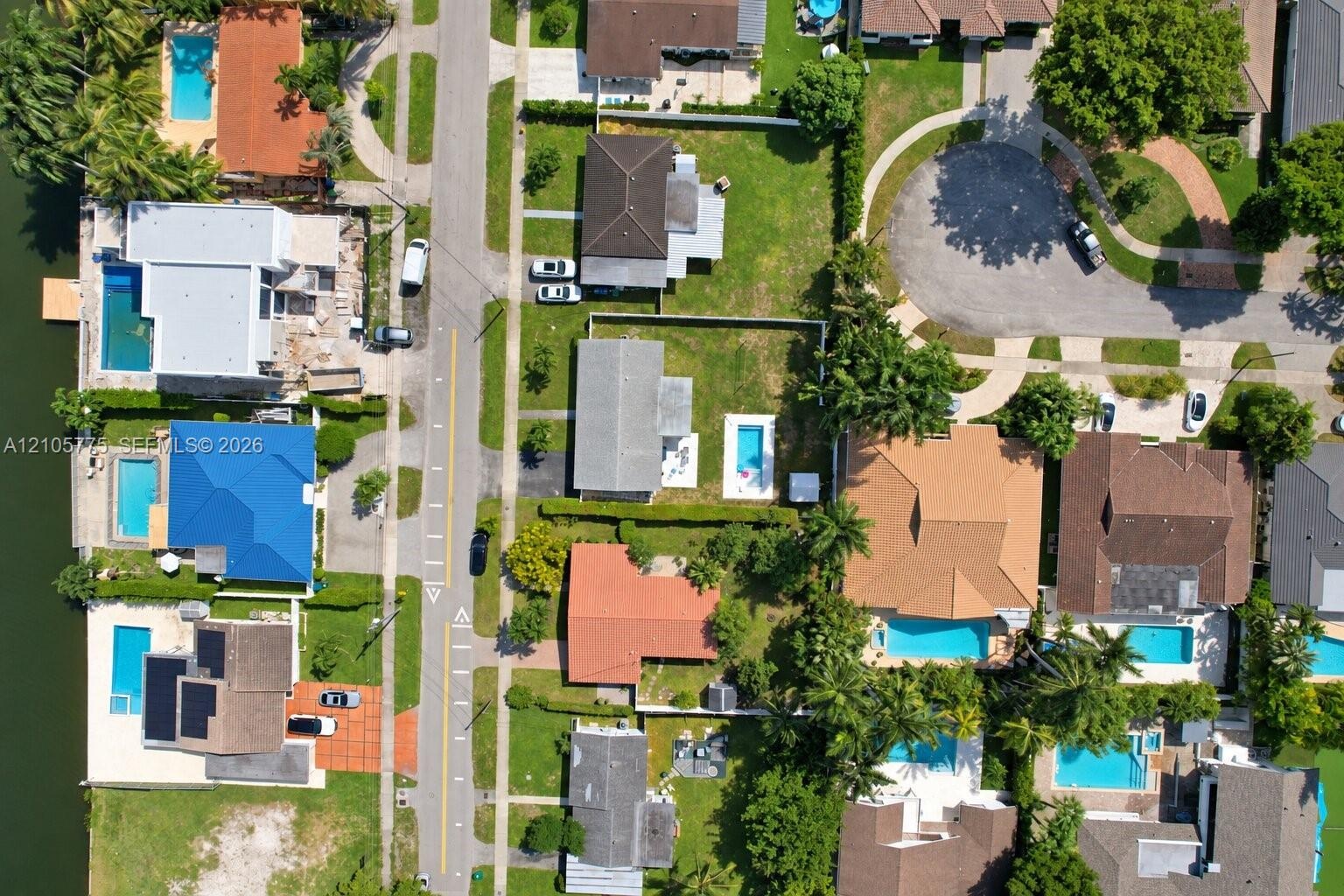Aerial view of a waterfront residential neighborhood featuring in-ground swimming pools, mature palm trees, and canal access