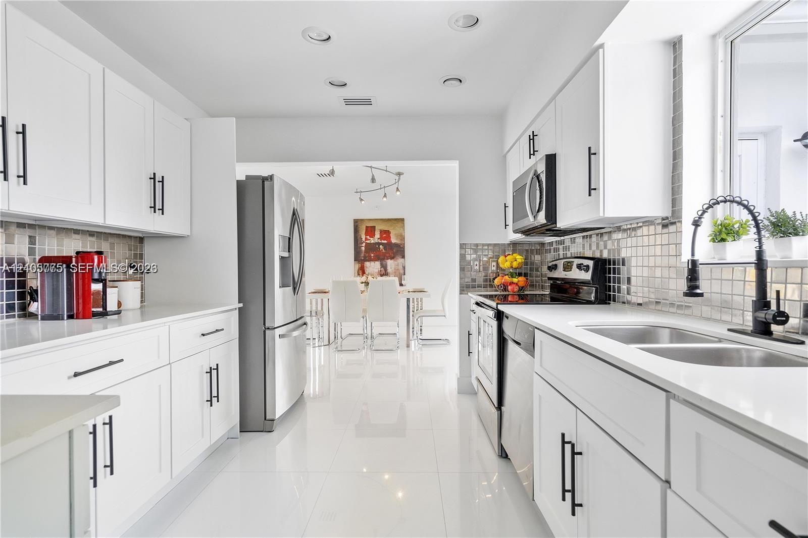 Kitchen featuring white shaker-style cabinetry, stainless steel appliances, tiled backsplash, dual-basin stainless steel sink with a matte black fauce