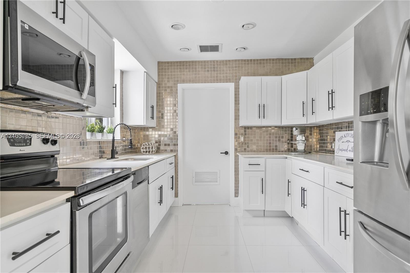 Kitchen featuring white cabinetry with matte black hardware, stainless steel appliances, a metallic mosaic tile backsplash, and gloss-finish floor til