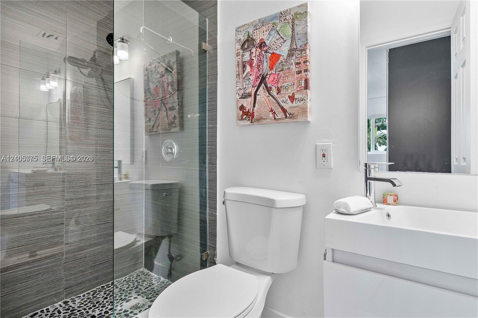 Bathroom featuring a frameless glass walk-in shower with horizontal tile surround and pebble tile flooring, white vanity with a rectangular integrated