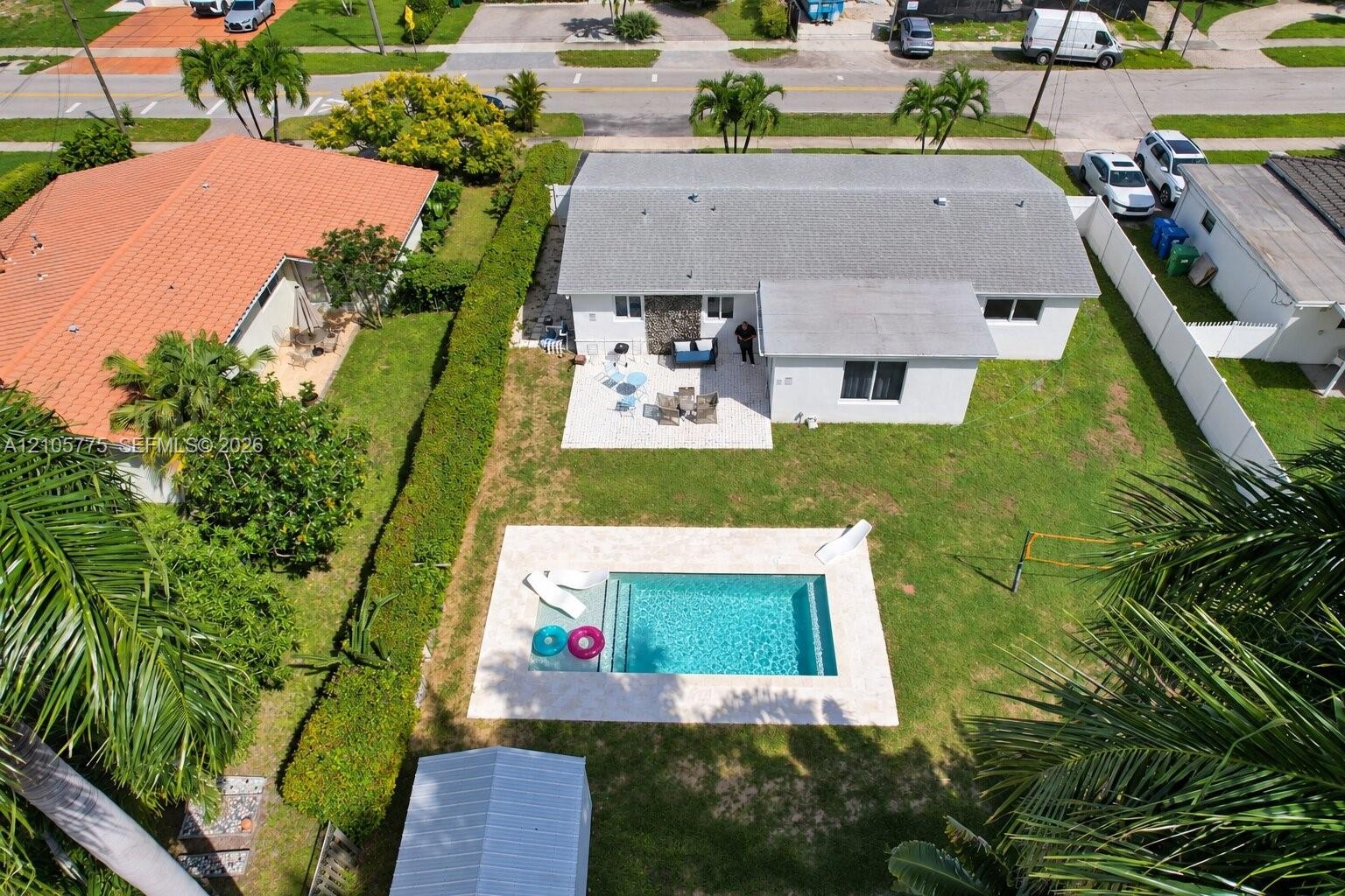Fenced backyard featuring an in-ground swimming pool, stone-finish pool deck, concrete patio, and stone exterior accent