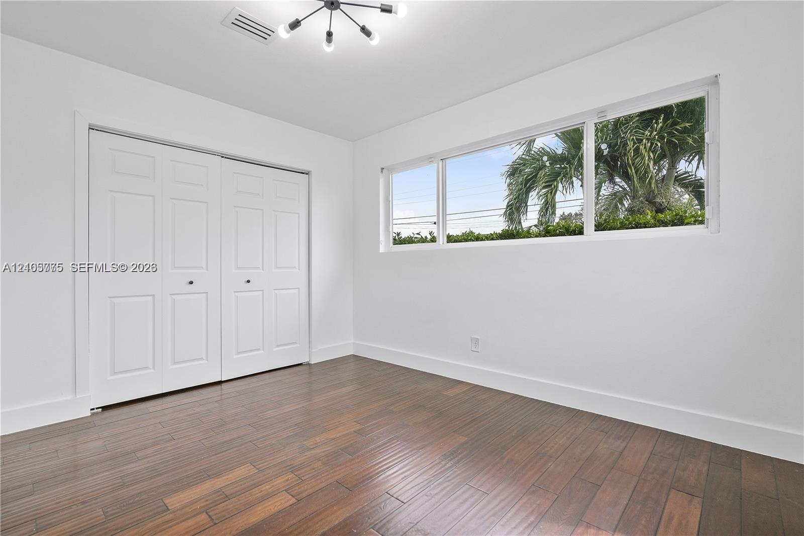 Room featuring dark-toned wood-finish flooring, a multi-arm modern light fixture, expansive horizontal window, and floor-to-ceiling built-in closet wi