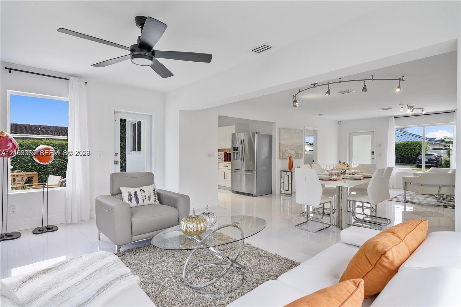 Open-concept interior featuring polished tile flooring, matte black ceiling fan, stainless steel refrigerator, and modern track lighting